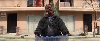 Movie still from “Magnolia” (1999), directed by Paul Thomas Anderson – A young man holding a plastic container in front of a building; Medium shot, Low angle