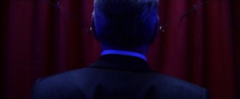 Movie still from “Magnolia” (1999), directed by Paul Thomas Anderson – A man in a black suit with blue lights around his neck; Close Up shot, Low angle