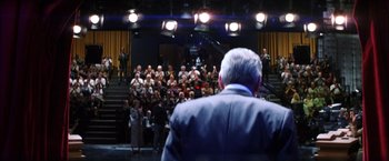 Movie still from “Magnolia” (1999), directed by Paul Thomas Anderson – An older man is standing in front of a group of people; Wide shot, High angle