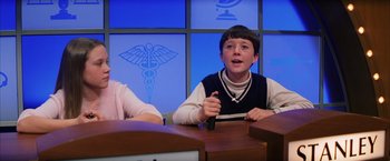 Movie still from “Magnolia” (1999), directed by Paul Thomas Anderson – A young boy sitting at a table in front of a medical sign; Medium shot, Low angle