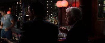 Movie still from “Magnolia” (1999), directed by Paul Thomas Anderson – A man sitting at a table in front of two other men; Medium shot, Over the shoulder angle