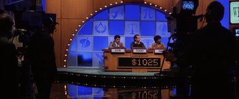 Movie still from “Magnolia” (1999), directed by Paul Thomas Anderson – Three people are sitting at a table in front of a sign; Medium shot, Over the shoulder angle