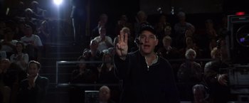 Movie still from “Magnolia” (1999), directed by Paul Thomas Anderson – A man in a crowd of people holding up a peace sign; Close Up shot, Over the shoulder angle