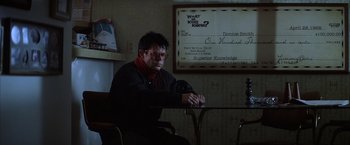 Movie still from “Magnolia” (1999), directed by Paul Thomas Anderson – A man sitting at a table in front of a check; Medium shot, Over the shoulder angle