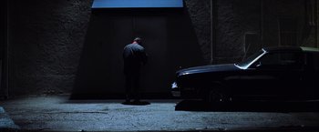Movie still from “Magnolia” (1999), directed by Paul Thomas Anderson – A man standing in front of a car in the dark next to a building; Wide shot, Low angle