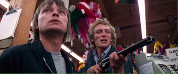 Movie still from “Magnum Force” (1973), directed by Ted Post – Two men standing next to each other holding a cell phone; Medium shot, Low angle