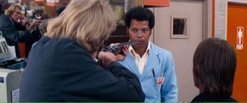 Movie still from “Magnum Force” (1973), directed by Ted Post – A man in a blue jacket is holding a gun; Medium shot, Over the shoulder angle