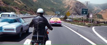 Movie still from “Magnum Force” (1973), directed by Ted Post – A man riding a motorcycle down a street next to a car; Wide shot, High angle