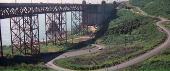 Movie still from “Magnum Force” (1973), directed by Ted Post – A view of a bridge from a hill with cars on it; Extreme Wide shot, High angle