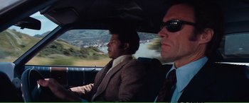 Movie still from “Magnum Force” (1973), directed by Ted Post – Two men in suits and ties driving in a car; Medium shot, Over the shoulder angle