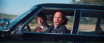 Movie still from “Magnum Force” (1973), directed by Ted Post – Two men in suits in the back seat of a car; Medium shot, Low angle