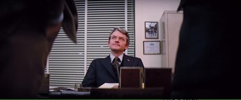 Movie still from “Magnum Force” (1973), directed by Ted Post – A man sitting at a desk in front of a laptop; Medium shot, Over the shoulder angle