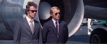 Movie still from “Magnum Force” (1973), directed by Ted Post – A man in a suit standing next to another man in a suit; Medium shot, Low angle