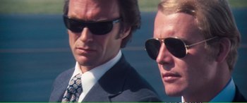 Movie still from “Magnum Force” (1973), directed by Ted Post – Two men in suits and sunglasses are standing next to each other; Close Up shot, Low angle
