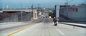 Movie still from “Magnum Force” (1973), directed by Ted Post – A person riding a motorcycle down the middle of a street; Extreme Wide shot, High angle