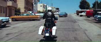 Movie still from “Magnum Force” (1973), directed by Ted Post – A man riding a motorcycle down a street; Wide shot, High angle