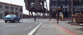 Movie still from “Magnum Force” (1973), directed by Ted Post – A person riding a motorcycle down a street near a bridge; Extreme Wide shot, High angle
