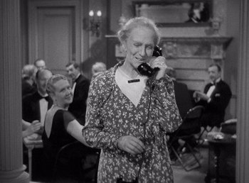 Movie still from “Make Way for Tomorrow” (1937), directed by Leo McCarey – An older woman talking on a phone in front of a group of people; Medium shot, High angle
