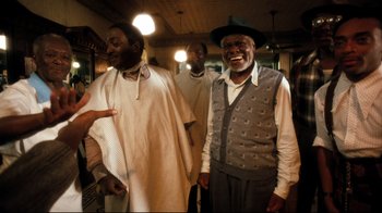 Movie still from “Malcolm X” (1992), directed by Spike Lee – A group of men standing next to each other in a room; Medium shot, Low angle