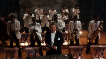 Movie still from “Malcolm X” (1992), directed by Spike Lee – A man in a white suit playing the xylophone in front of a group of men; Extreme Wide shot, High angle