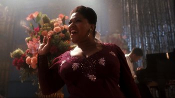 Movie still from “Malcolm X” (1992), directed by Spike Lee – A woman in a maroon dress is singing; Medium shot, Low angle
