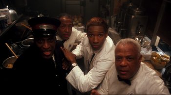 Movie still from “Malcolm X” (1992), directed by Spike Lee – A group of men standing next to each other in a kitchen; Medium shot, Low angle