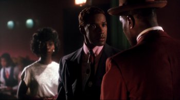 Movie still from “Malcolm X” (1992), directed by Spike Lee – A man wearing a suit and tie talking to two other men; Close Up shot, Over the shoulder angle