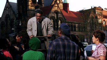 Movie still from “Malcolm X” (1992), directed by Spike Lee – A group of people standing around a building; Medium shot, Over the shoulder angle