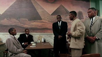 Movie still from “Malcolm X” (1992), directed by Spike Lee – A group of men standing around a wooden table; Wide shot, Over the shoulder angle