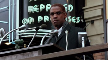 Movie still from “Malcolm X” (1992), directed by Spike Lee – A man is speaking at a podium in front of microphones; Close Up shot, Low angle