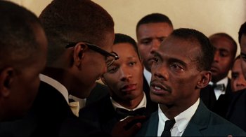 Movie still from “Malcolm X” (1992), directed by Spike Lee – A group of men standing around each other in a room; Close Up shot, Over the shoulder angle