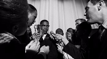 Movie still from “Malcolm X” (1992), directed by Spike Lee – A black and white photo of a group of men holding microphones; Medium shot, Over the shoulder angle