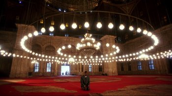 Movie still from “Malcolm X” (1992), directed by Spike Lee – A man in a suit sitting on the ground in a large room; Extreme Wide shot, High angle