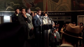 Movie still from “Malcolm X” (1992), directed by Spike Lee – A group of people standing in front of microphones; Medium shot, High angle