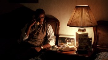 Movie still from “Malcolm X” (1992), directed by Spike Lee – A man sitting in a chair talking on the phone; Medium shot, High angle