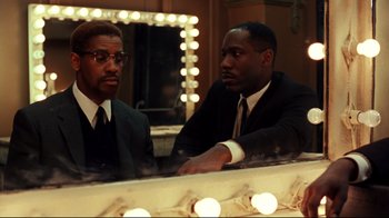 Movie still from “Malcolm X” (1992), directed by Spike Lee – Two men in suits are looking at each other in front of a vanity mirror; Medium shot, Over the shoulder angle