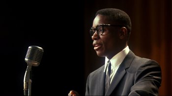Movie still from “Malcolm X” (1992), directed by Spike Lee – A man in a suit and tie is talking into a microphone; Close Up shot, Low angle