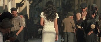 Movie still from “Malena” (2000), directed by Giuseppe Tornatore – A woman in a white dress is walking down the street; Medium shot, Over the shoulder angle