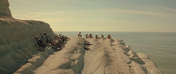 Movie still from “Malena” (2000), directed by Giuseppe Tornatore – A group of people sitting on top of a sandy beach; Extreme Wide shot, High angle