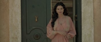 Movie still from “Malena” (2000), directed by Giuseppe Tornatore – A woman in a pink robe standing in front of a green door; Medium shot, Over the shoulder angle