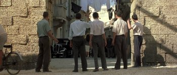 Movie still from “Malena” (2000), directed by Giuseppe Tornatore – A group of men standing next to each other on a street; Wide shot, Low angle