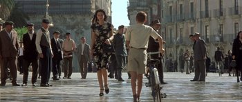Movie still from “Malena” (2000), directed by Giuseppe Tornatore – A woman walking down the street with a bicycle; Wide shot, Low angle