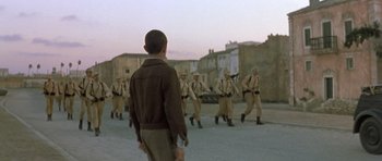 Movie still from “Malena” (2000), directed by Giuseppe Tornatore – A group of men in uniform marching down a street; Wide shot, Low angle