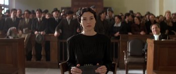 Movie still from “Malena” (2000), directed by Giuseppe Tornatore – A woman sitting in a chair in front of a group of people; Medium shot, Low angle