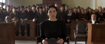 Movie still from “Malena” (2000), directed by Giuseppe Tornatore – A woman in a black dress is holding a book in front of a group of people; Medium shot, Low angle