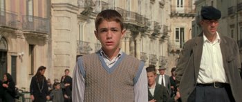 Movie still from “Malena” (2000), directed by Giuseppe Tornatore – A young man in a vest standing in front of a building; Medium shot, Low angle
