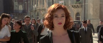 Movie still from “Malena” (2000), directed by Giuseppe Tornatore – A woman with red curly hair is standing in front of a group of people; Close Up shot, Over the shoulder angle