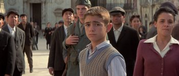 Movie still from “Malena” (2000), directed by Giuseppe Tornatore – A young boy standing in front of a group of men; Medium shot, Low angle
