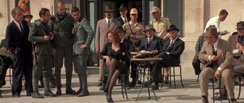 Movie still from “Malena” (2000), directed by Giuseppe Tornatore – A group of men and a woman sitting on a sidewalk; Wide shot, Low angle