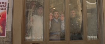 Movie still from “Malena” (2000), directed by Giuseppe Tornatore – A group of people standing behind a glass window; Medium shot, Low angle
